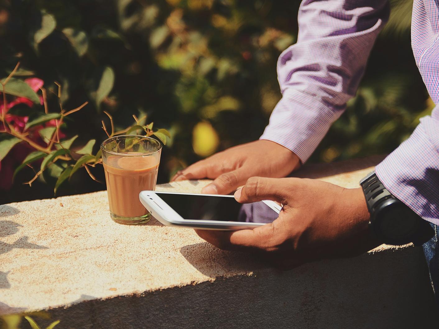 Man holding a mobile phone next to a glass on a sunny day