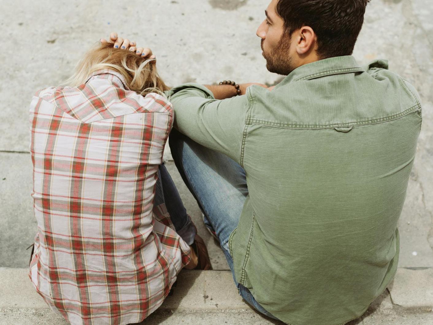 Man and woman sitting on pavement. Woman has her head in her hands