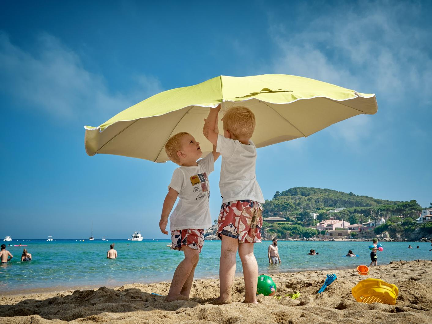 Two children under a yellow umbrella on a sunny beach