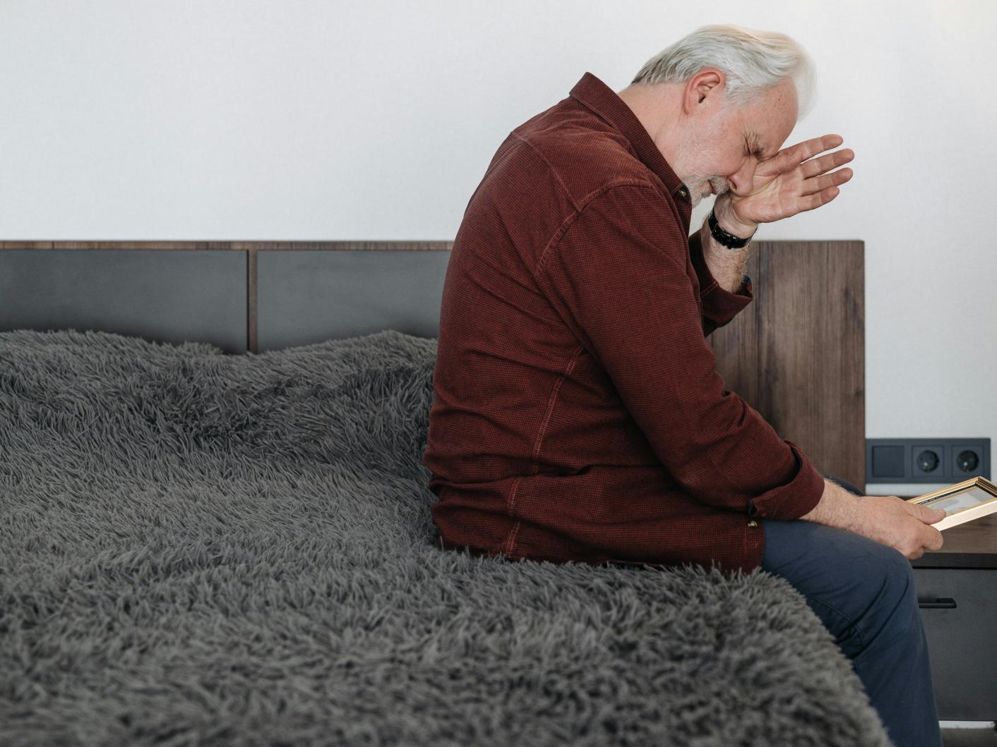 Photo of man crying whilst sitting on a bed looking at a photo